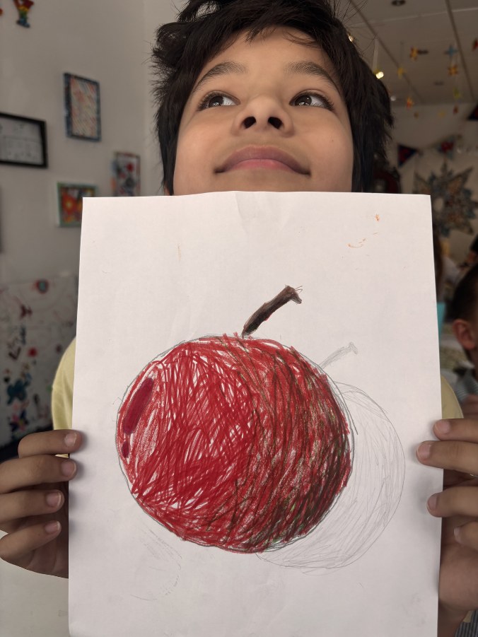 Child holding up their crayon drawing of an apple
