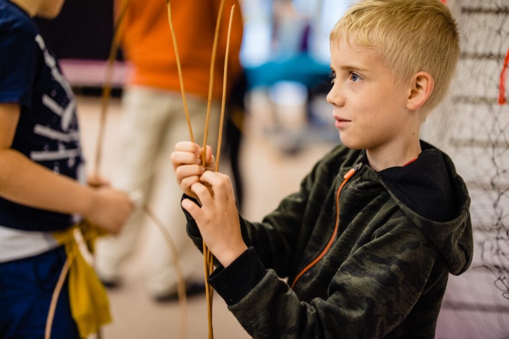 An older child focused on weaving a willow sculpture